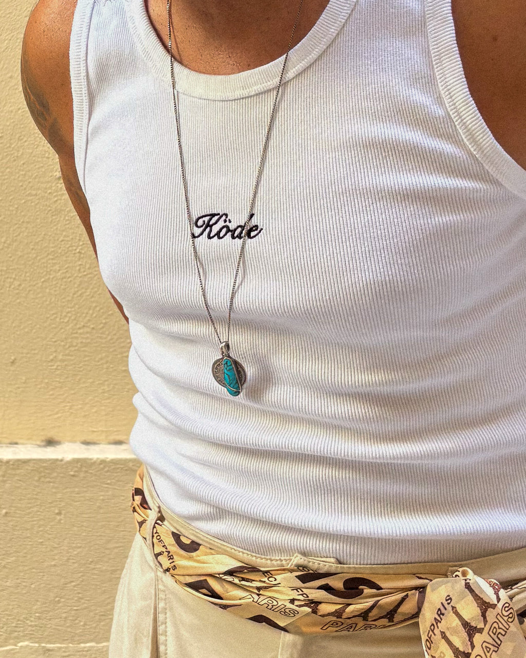 Detalle del bordado KÖDE en camiseta de tirantes blanca slim fit, tejido canalé y accesorios metálicos.